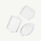 Three empty, white ceramic baking dishes of different shapes are positioned on a light background.