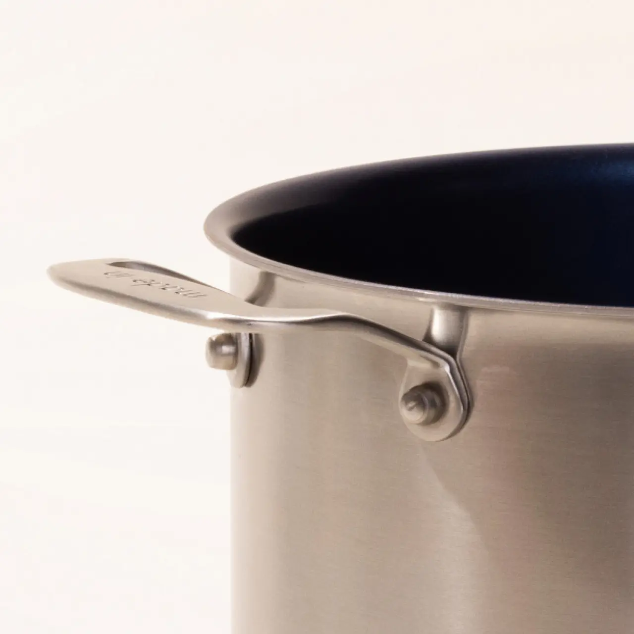 A close-up of a stainless steel pot with a blue interior and a visible brand name on the handle.