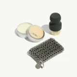 A small collection of grooming products includes a metal mesh pouch, a tin of cream, and a brush with a round top.