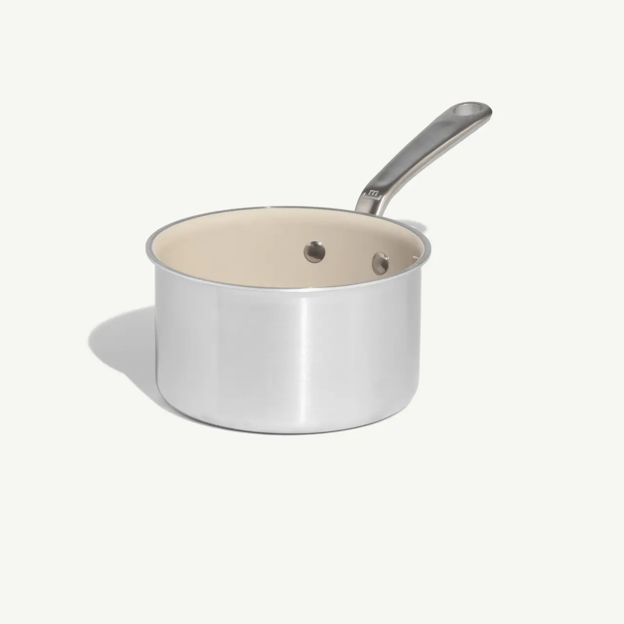 A stainless steel saucepan with a smooth exterior and a white interior sits against a light background.