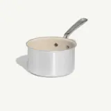 A stainless steel saucepan with a smooth exterior and a white interior sits against a light background.