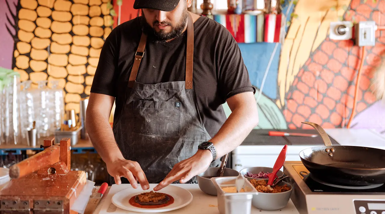 A focused chef is garnishing a dish in a vibrant kitchen setting.