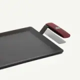 A rectangular cast iron griddle with a red handle is shown against a plain background.