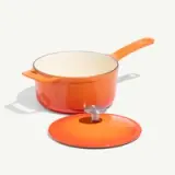 An orange saucepan with a matching lid set to the side on a light-colored background.