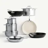 A collection of various cookware, including pots, pans, and a wok, arranged in an artistic display on a light background.