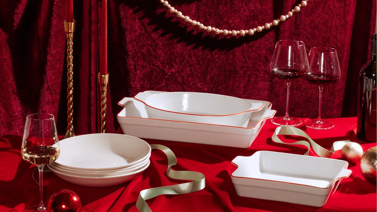 An elegant dinner setting with red theme featuring wine glasses, ceramic dishes, gold accents, and festive decorations on a table.