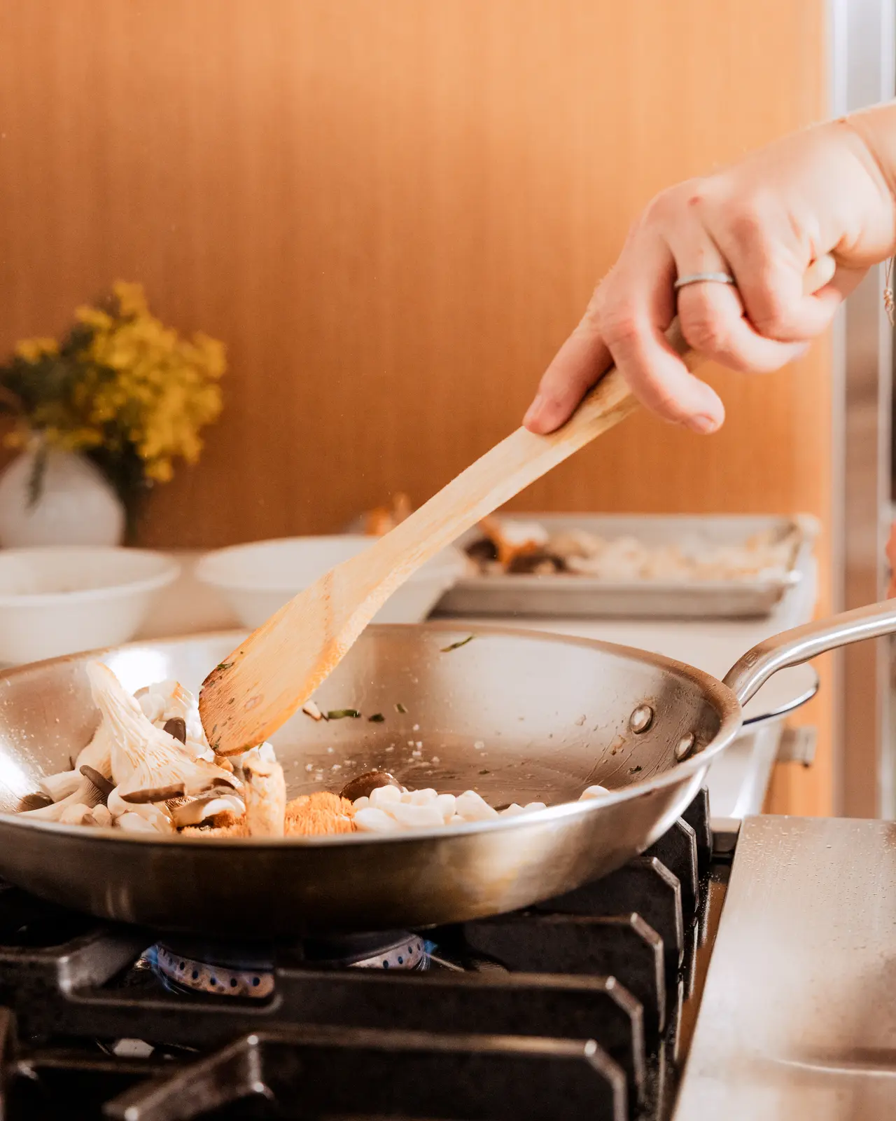 A person's hand is sautéing mushrooms and other ingredients in a frying pan over a stovetop.