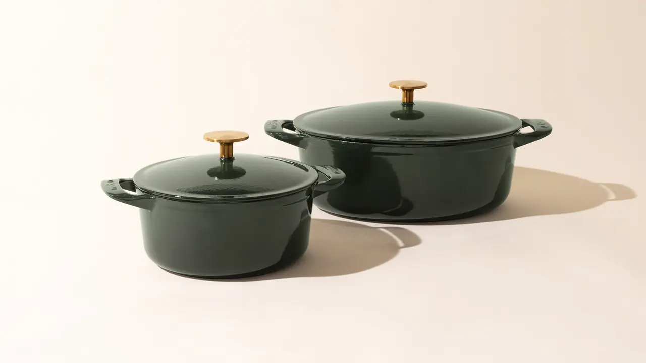 Two dark-colored cooking pots with lids and contrasting handles sit against a neutral background.