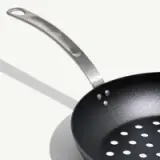 A non-stick frying pan with a stainless steel handle casts a shadow on a light-colored surface.