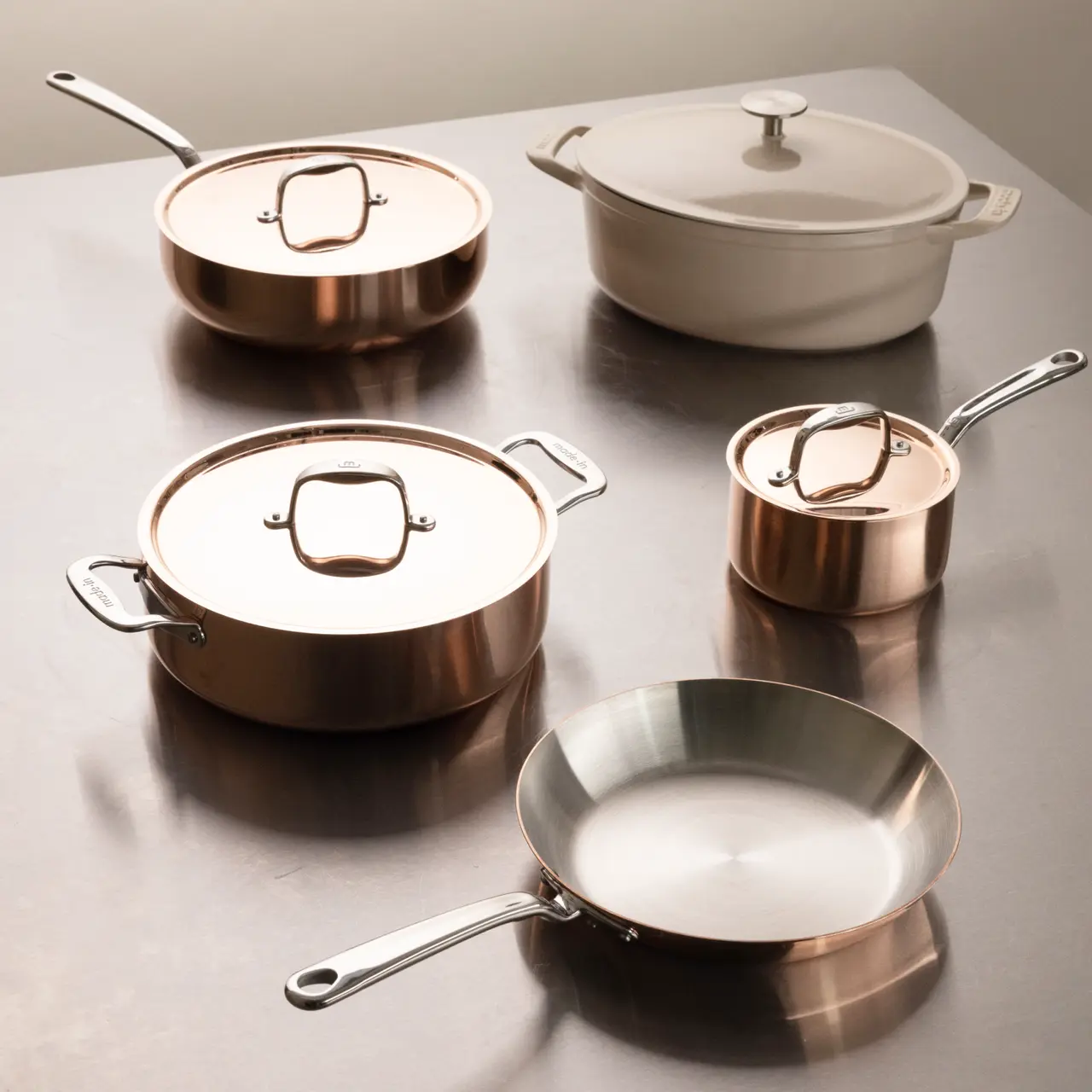 A collection of polished copper cookware is neatly arranged on a reflective surface.