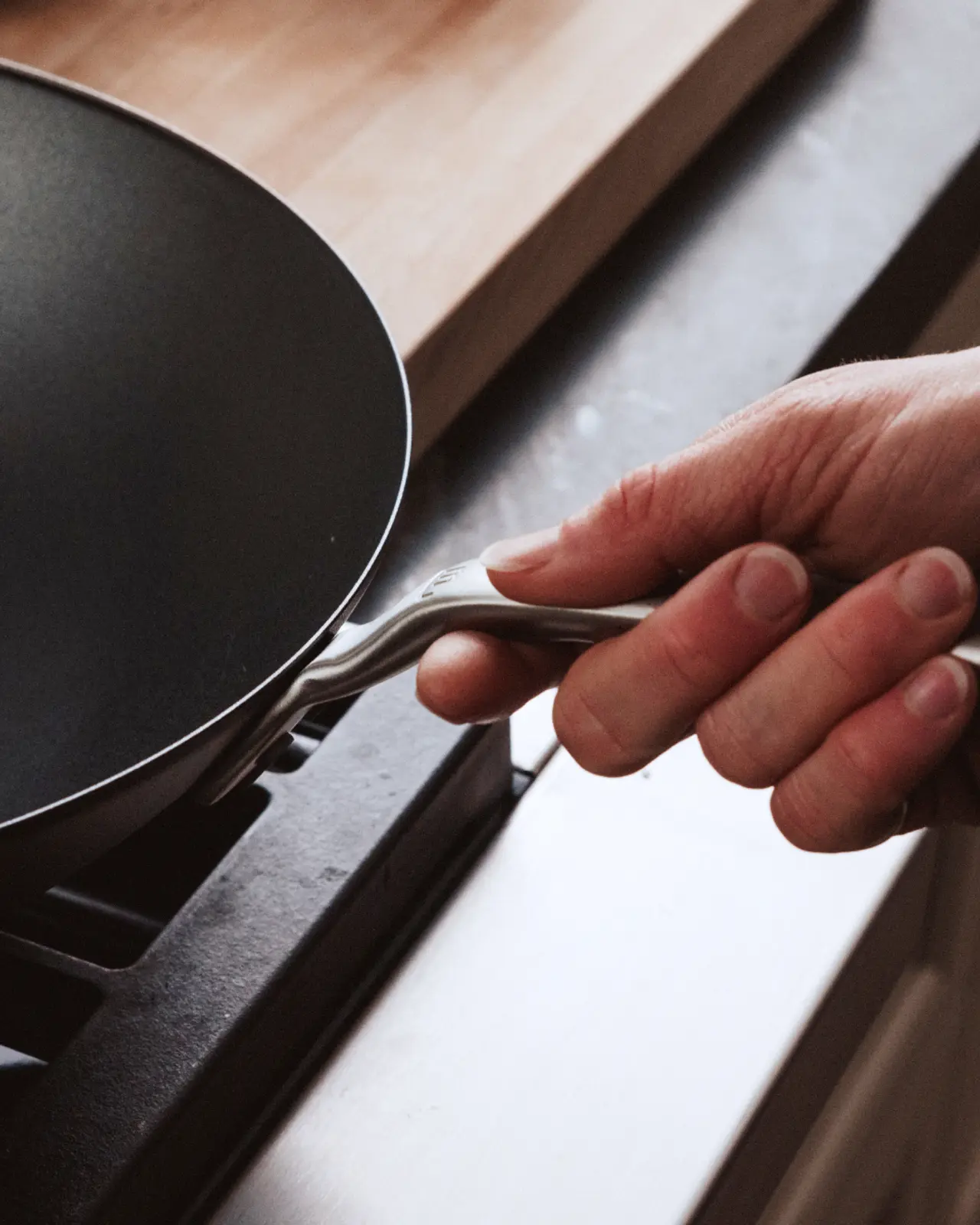 A hand is gripping the handle of a frying pan over a stovetop.