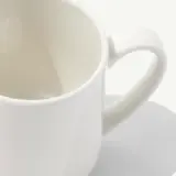 A plain white ceramic mug is resting on a light gray surface.