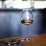 A glass of white wine on a wooden table with blurred background of a bar setting.