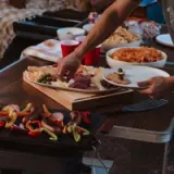 A person reaches for food from an assorted charcuterie board amidst a spread of snacks on a table.