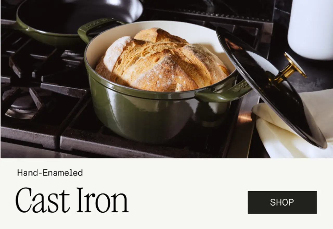 A green hand-enameled cast iron Dutch oven is filled with freshly baked bread, placed on a stove top.