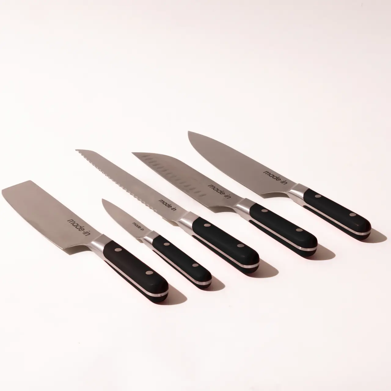 A set of five different kitchen knives with black handles arranged in a row on a light background.