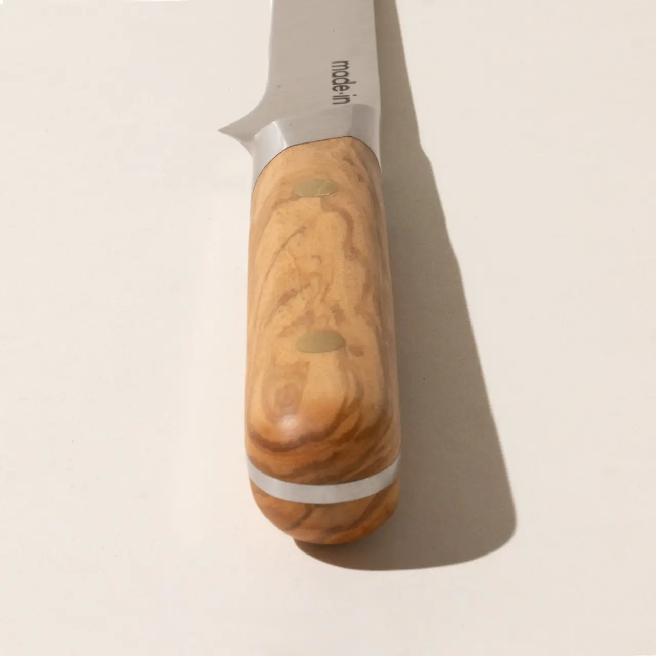 A stainless steel paring knife with a polished wooden handle lies on a light surface casting a slight shadow.