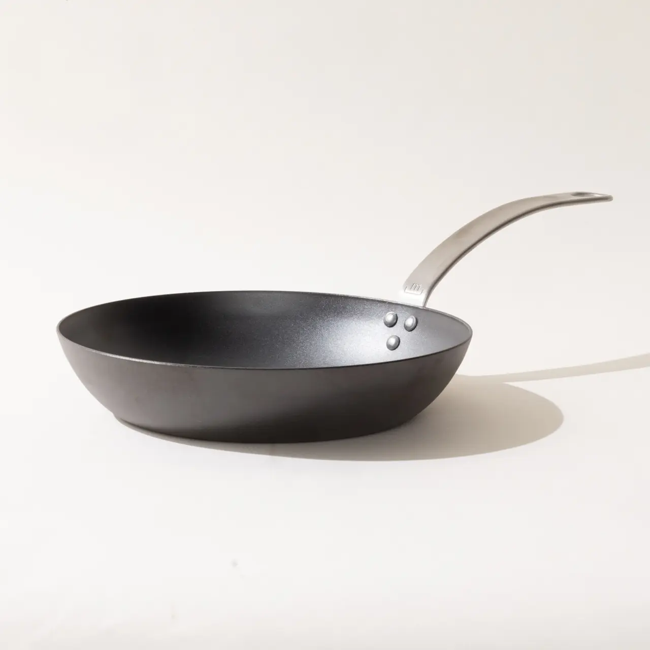 A black frying pan with a silver handle positioned on a plain background showcasing its profile.