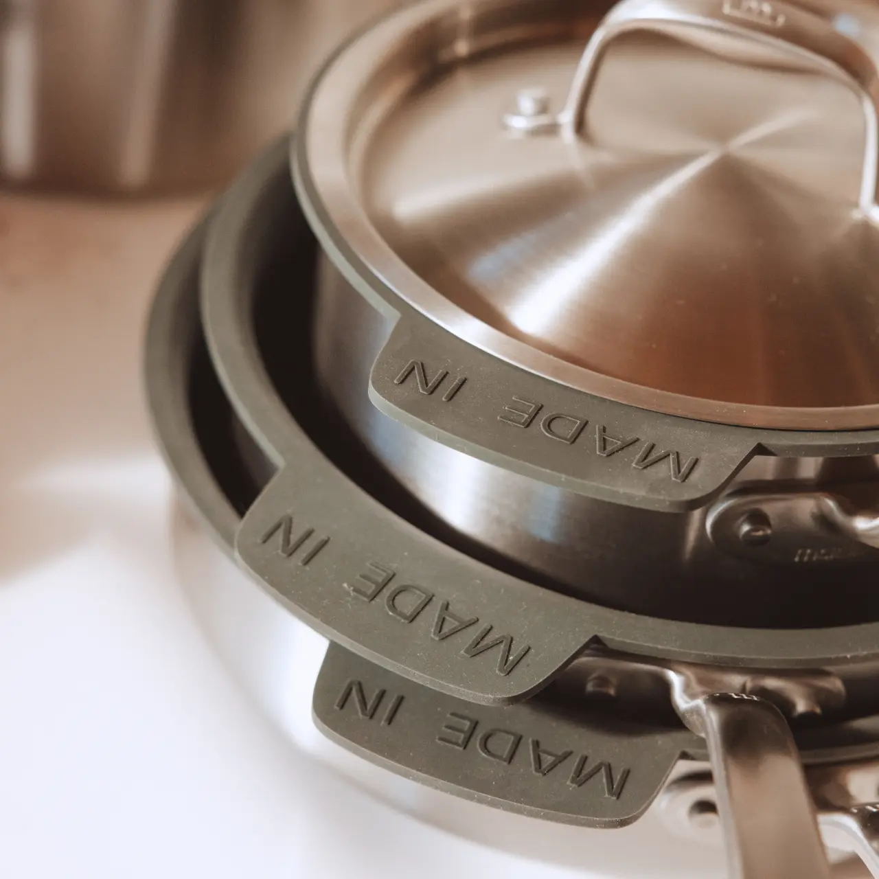 Stacked cookware with grey silicone handles and lids, featuring the inscription "MADE IN."