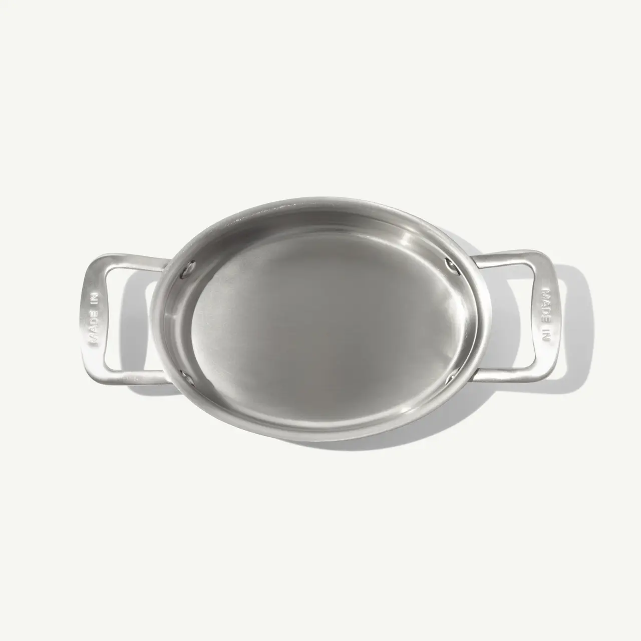 An oval stainless steel dish with two handles is shown from above on a light background.