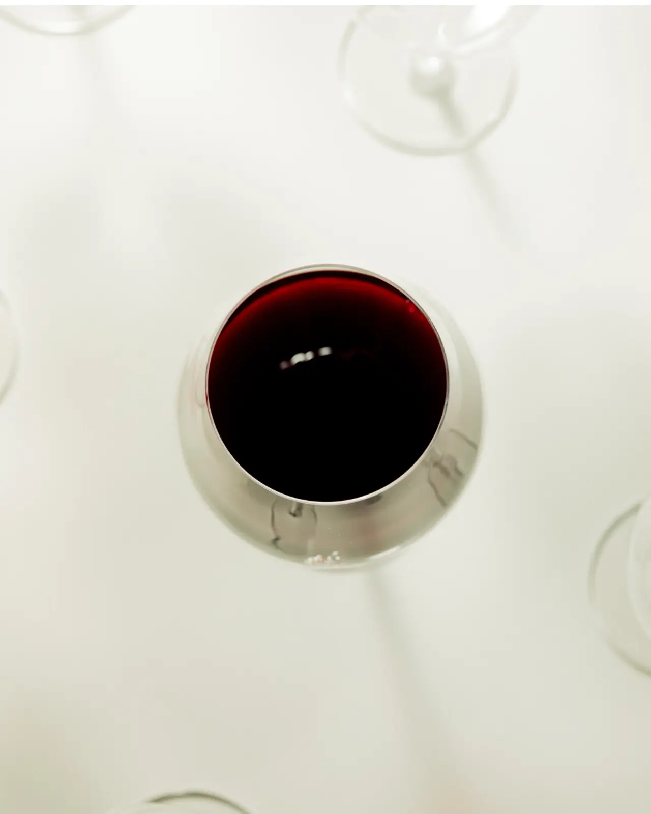 A glass of red wine is viewed from above, with the edges of other stemware glasses visible in the background.