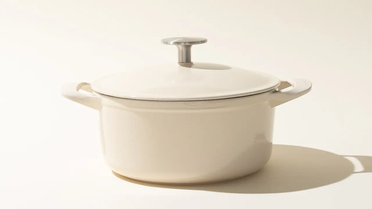 A neutral-colored cooking pot with a lid, placed on a plain surface casting a soft shadow.