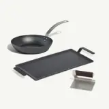A black skillet, a flat griddle, and a metal spatula are arranged on a light background.