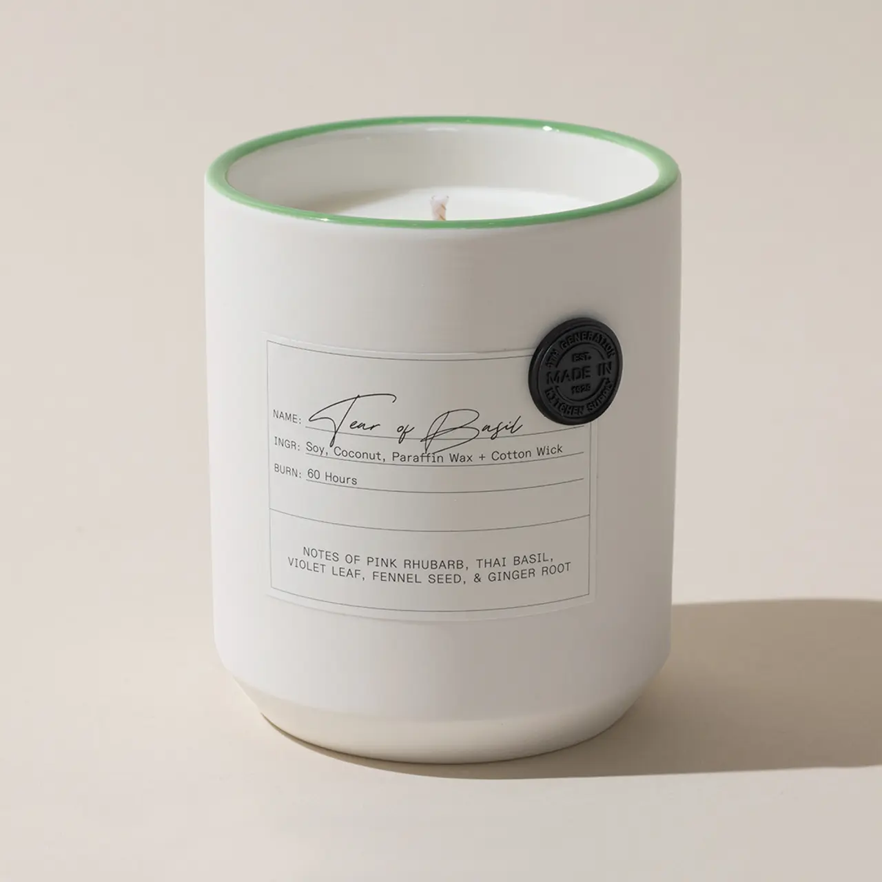 A scented candle with a description label and a green rim sits against a neutral background.