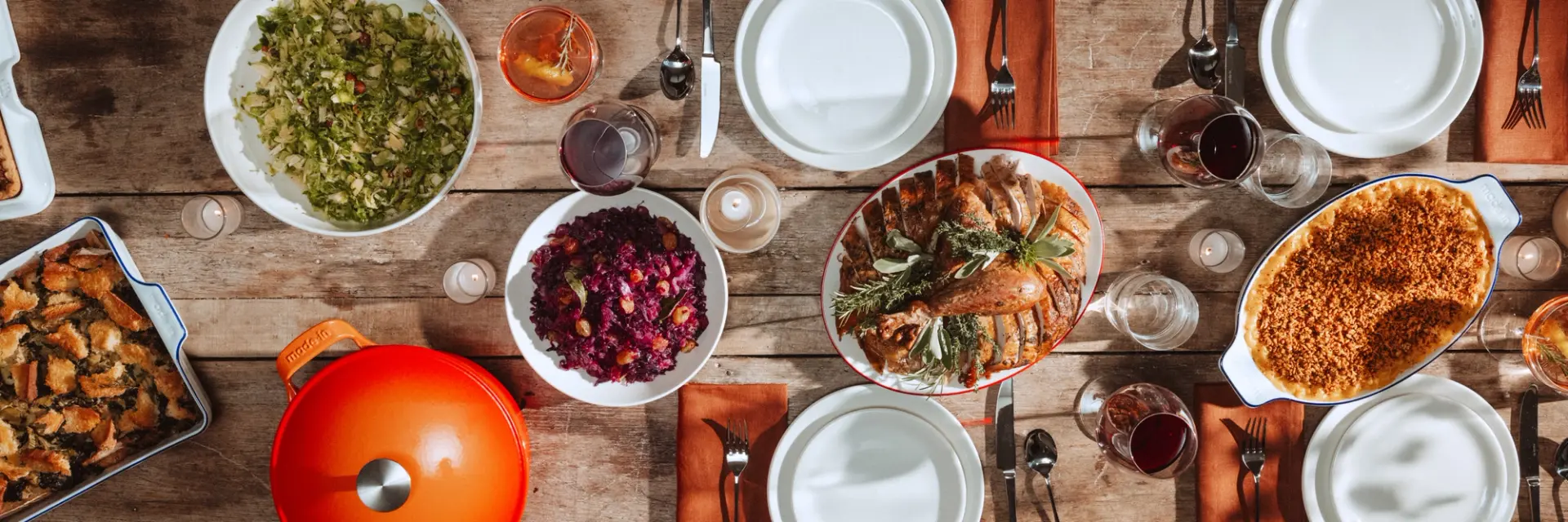 A variety of dishes and plates are neatly arranged on a wooden table, suggesting a communal meal setting.