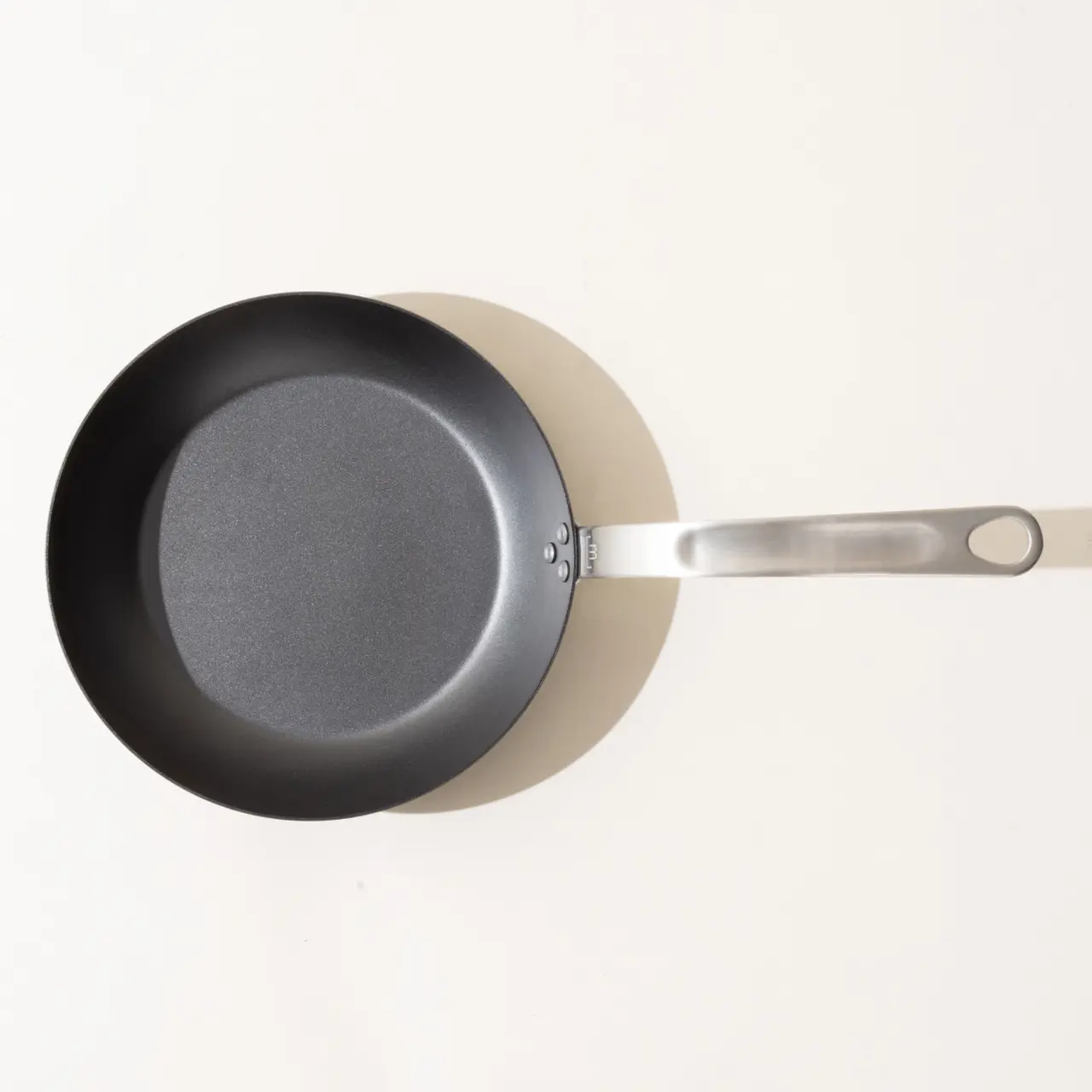 A non-stick frying pan with a silver handle on a light background, viewed from above.