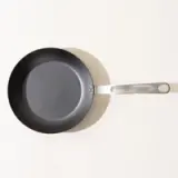 A non-stick frying pan with a silver handle on a light background, viewed from above.