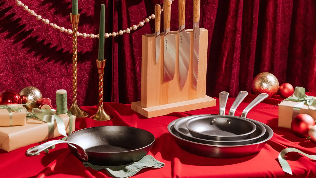 A festive holiday display with a variety of cookware, including pans and kitchen utensils, surrounded by Christmas decorations and gifts on a red tablecloth.
