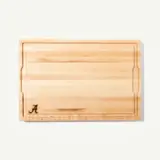 A wooden cutting board with a smooth, striped surface and a decorative initial "A" engraved at one corner.