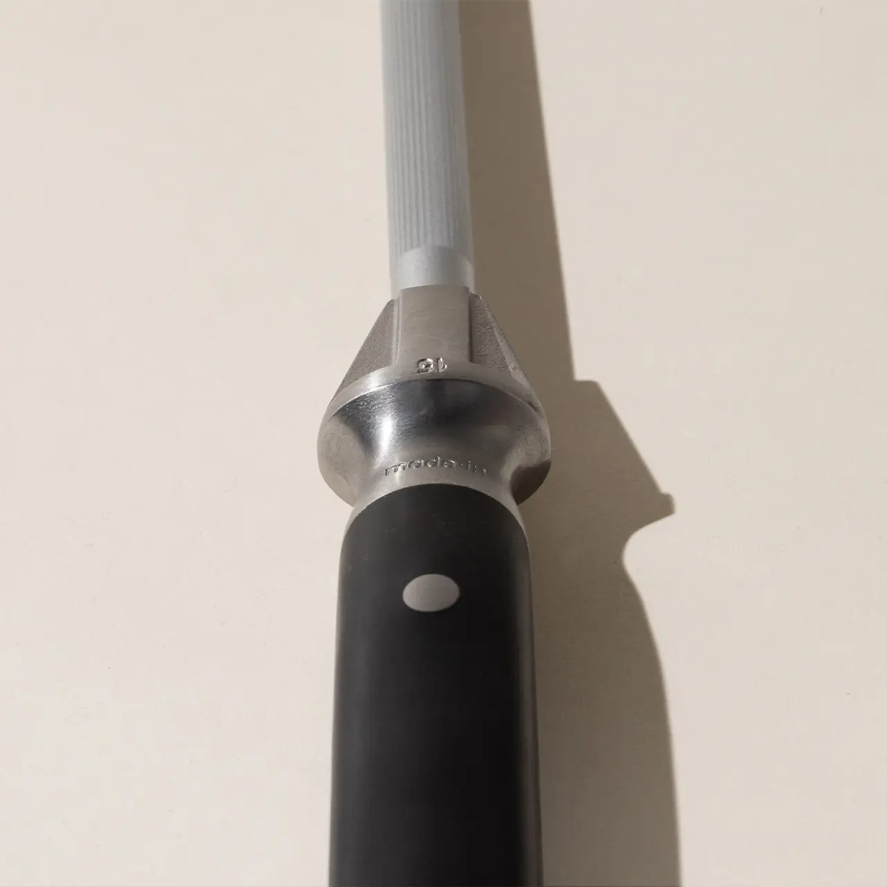 A close-up of the head of a reflex hammer with a metallic finish and a black handle casting a soft shadow on a neutral background.