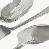 Three stainless steel serving utensils, including a slotted spoon, an angled spatula, and a regular spoon, are displayed against a light background.