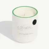 White candle in a ceramic holder with green trim, labeled "Teton Brûlé" and detailing scent notes and burn time.