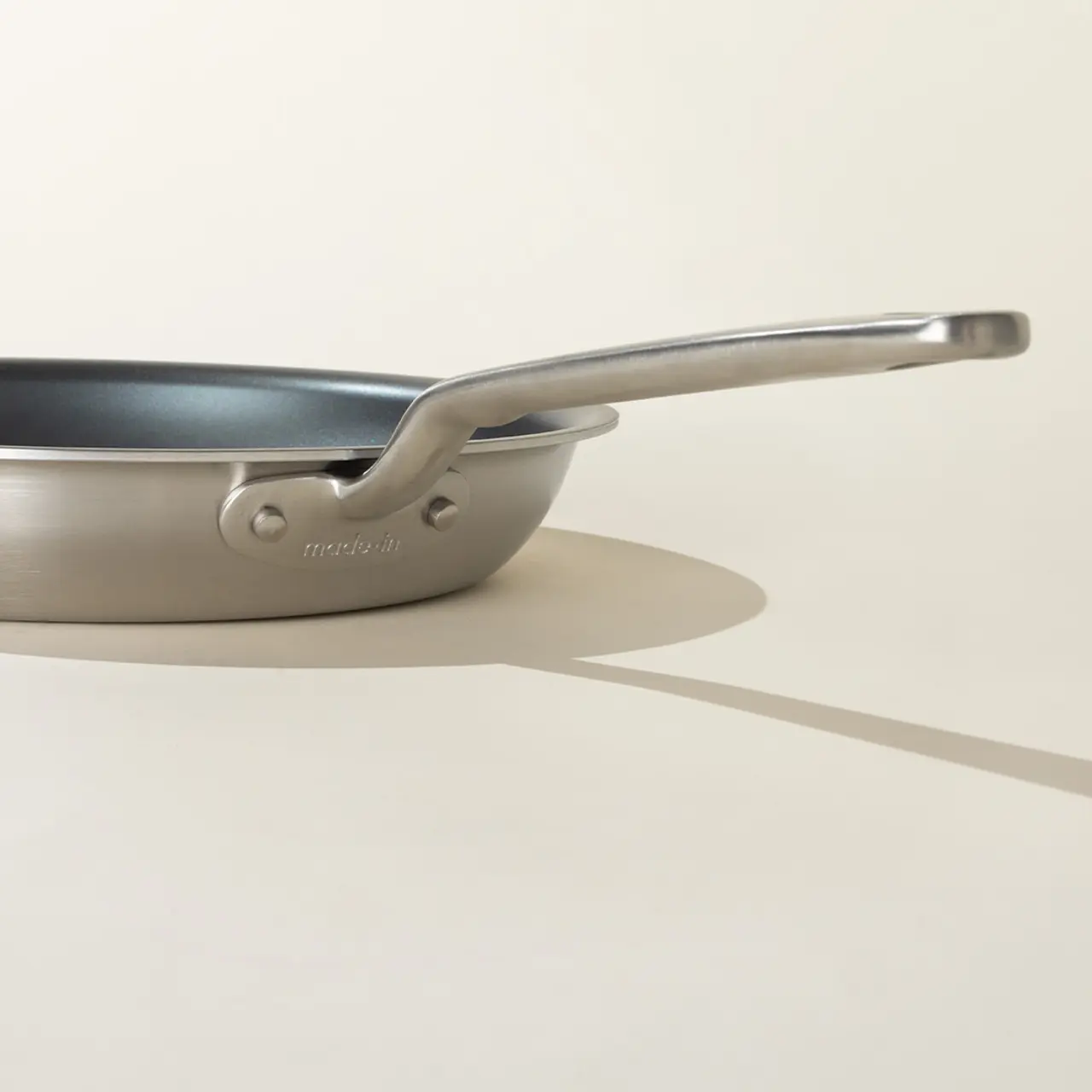 A stainless steel frying pan casts a long shadow on a light-colored background.