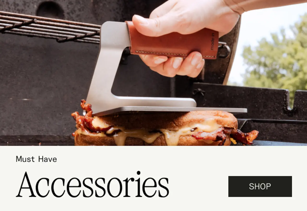 A hand grips a sleek, metallic grilling accessory over a hearty sandwich with bacon and cheese.