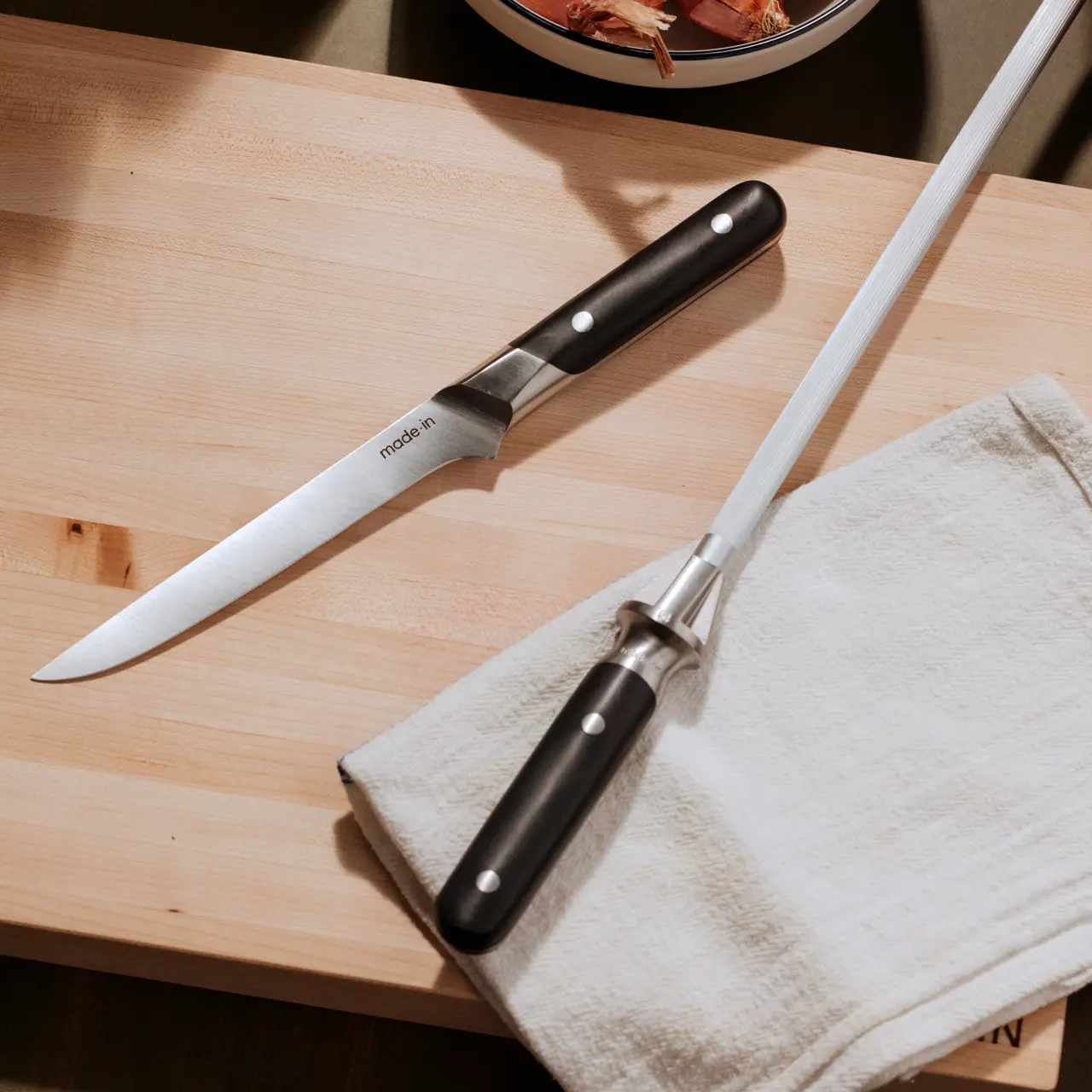 A chef's knife and a paring knife are placed on a wooden surface next to a folded kitchen towel.