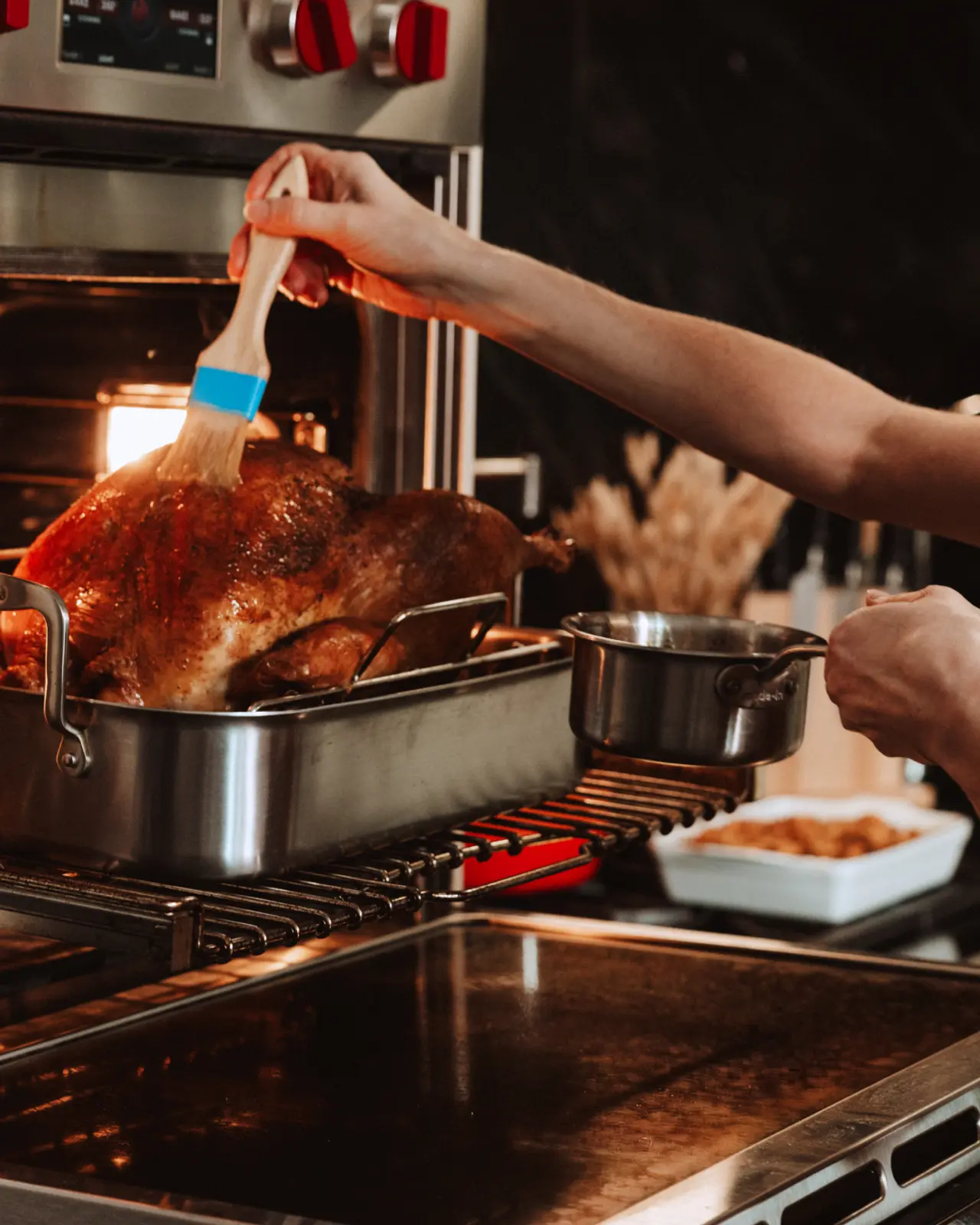 A person is brushing a golden-brown roasted turkey with glaze in an oven.