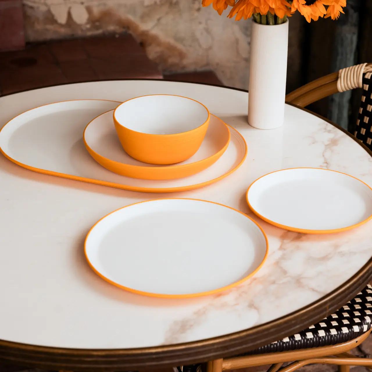 A set of orange-rimmed white dishes arranged neatly on a round marble table.