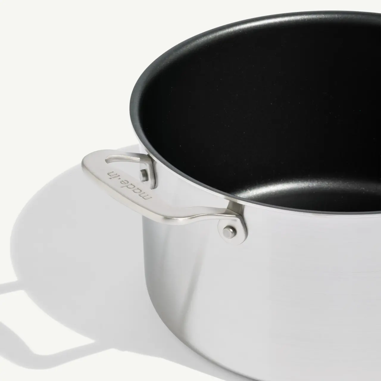 A close-up of a saucepan with a black interior and a steel handle casting a shadow against a light background.