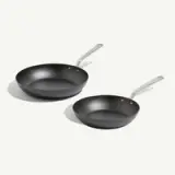 Two non-stick frying pans of different sizes with sleek metallic handles are positioned side by side.