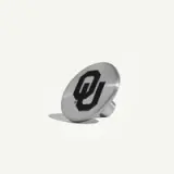A round, metallic button displays a black Oklahoma University logo on its surface.