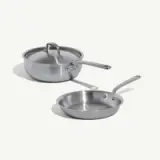 A stainless steel saucepan with a lid and a skillet are displayed together on a light background.
