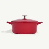 A red enameled cast iron Dutch oven with a lid and handles on both sides is displayed against a plain background.
