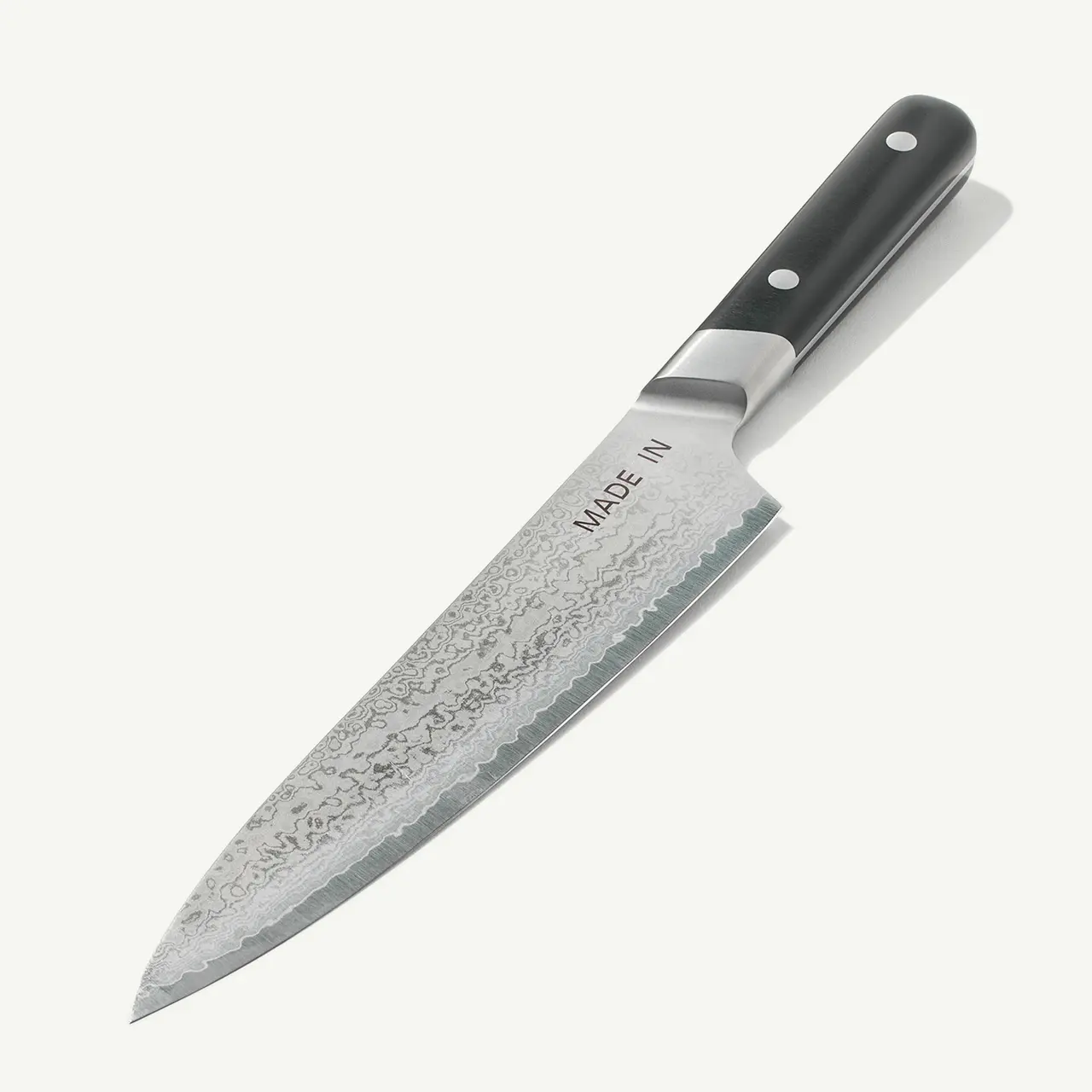 A chef's knife with a textured blade and a black handle labeled "MADE IN" is shown against a white background.