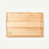A wooden cutting board featuring a subtle engraved letter "N" in one corner.