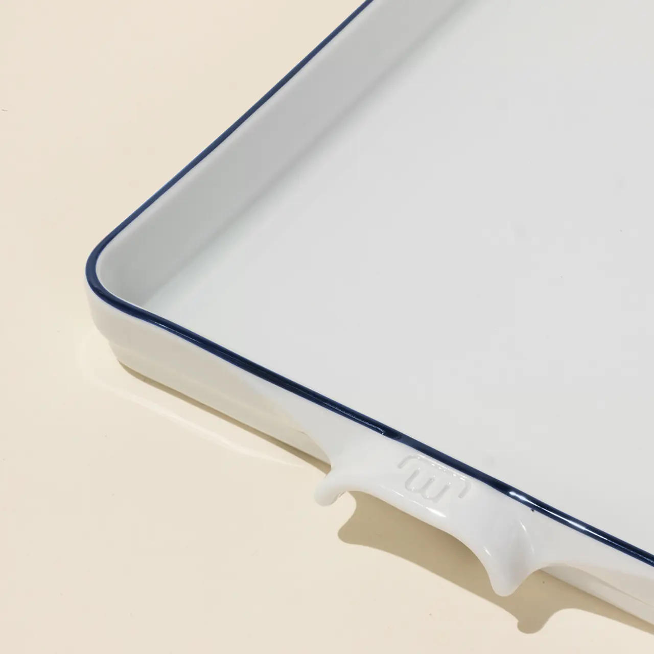 A close-up of a white rectangular ceramic dish with a blue rim on a pale background.