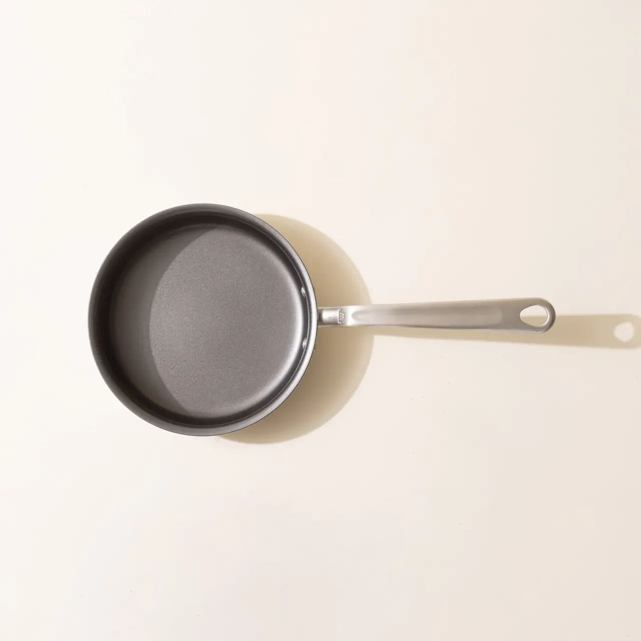 A new frying pan with a silver handle is pictured from above on a neutral background.
